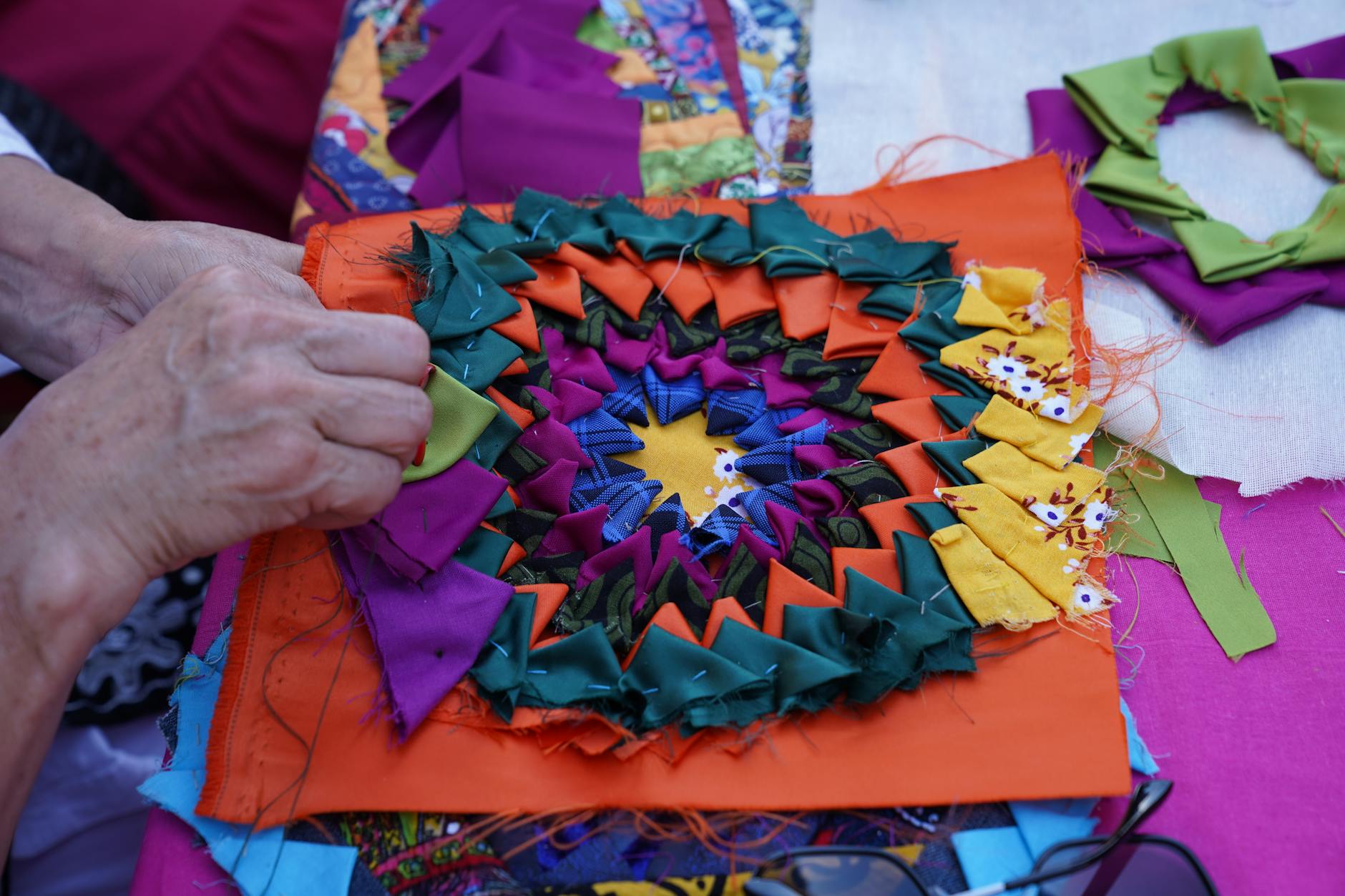 Dłonie układają kolorową patchworkową kompozycję z materiałowych skrawków