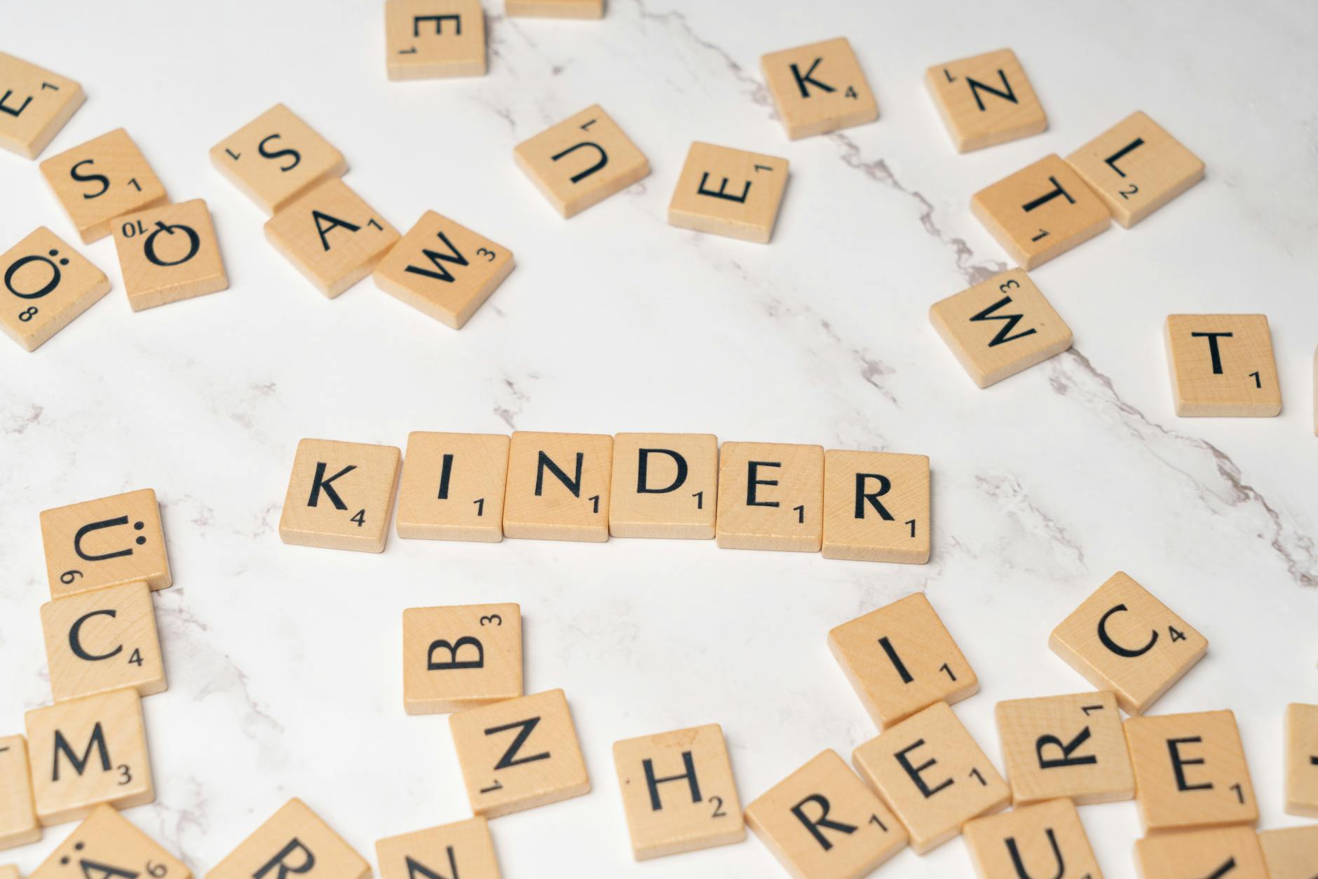 Kafelki Scrabble układające się w słowo Kinder na marmurowym tle