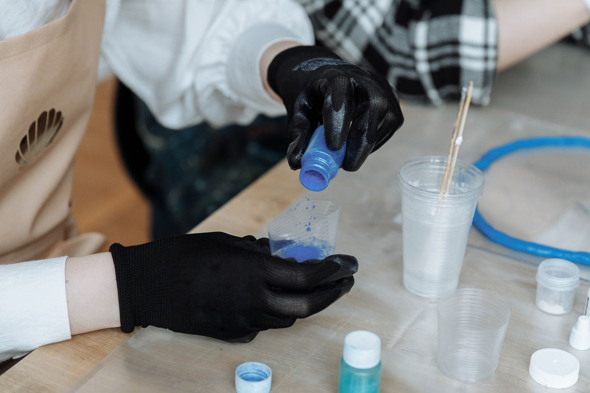 Dłonie w rękawiczkach mieszają kolorowe pigmenty w plastikowych kubkach